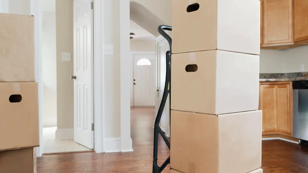 Hoher Stapel Umzugskartons auf einer Sackkarre im Flur einer Wohnung mit Holzboden und offenen Türen.