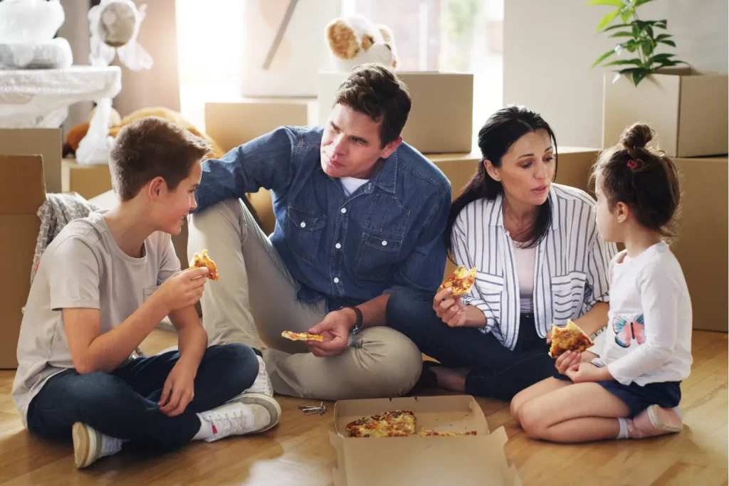 Familie isst gemeinsam Pizza auf dem Boden als Belohnung während des Umzugs.