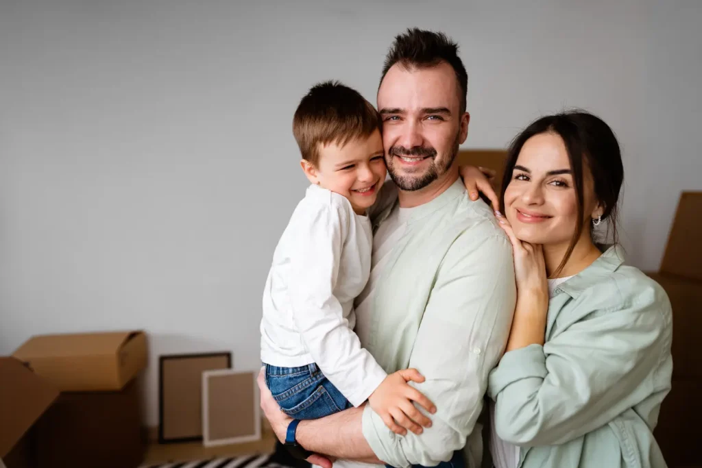 Glückliche dreiköpfige Familie lächelt zufrieden nach dem erfolgreichen Umzug in die neue Wohnung.